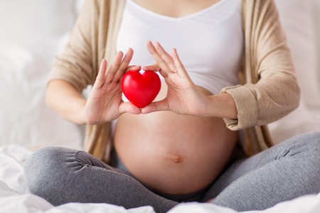 close up of pregnant woman with red heart in bedの写真素材