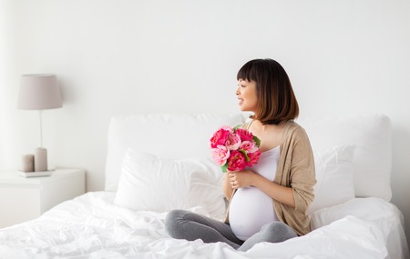 happy asian pregnant woman with flowers in bed