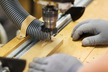 carpenter with drill press and board at workshop