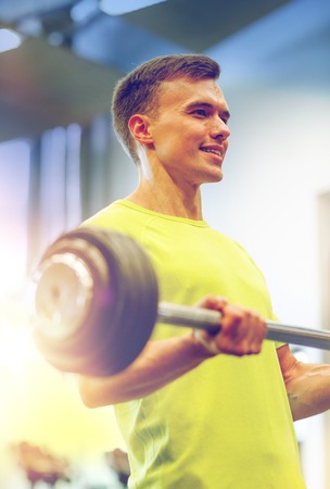 smiling man doing exercise with barbell in gymの写真素材