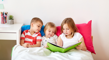 little kids reading book in bed at homeの写真素材