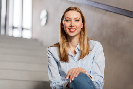 happy smiling woman or student sitting on stairsの写真素材