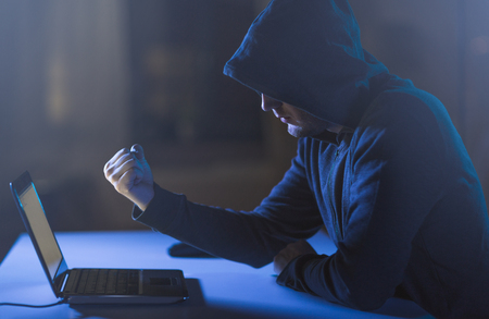 hacker showing fist to laptop in dark roomの写真素材