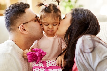 parents kissing little daughter with birthday giftの写真素材