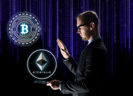 business, cryptocurrency and future technology concept - businessman with transparent tablet pc computer and virtual bitcoin and ethereum holograms over ultra violet binary code on black backgroundの写真素材