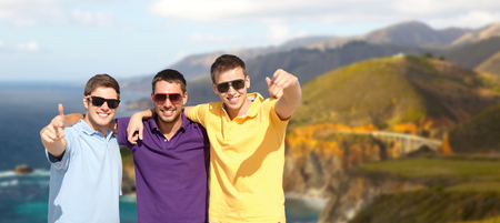travel, tourism and male friendship concept - group of friends hugging over bixby creek bridge on...