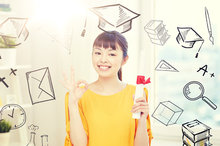 people, education, school, graduation and learning concept - happy asian young woman student with diploma scroll at home showing ok hand sign with doodlesの写真素材