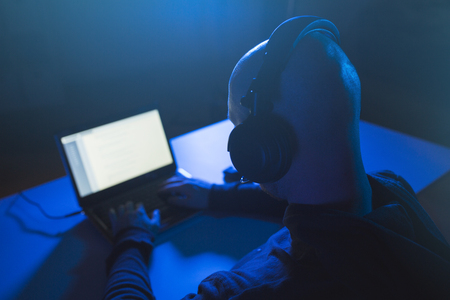 hacker with headset typing on laptop in dark roomの写真素材