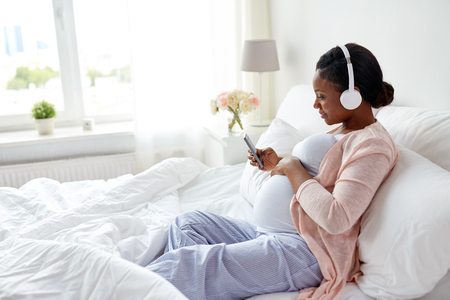 pregnant woman in headphones with smartphoneの写真素材