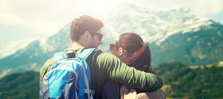 travel, tourism and people concept - happy couple with backpacks hugging over alps mountains backgroundの写真素材