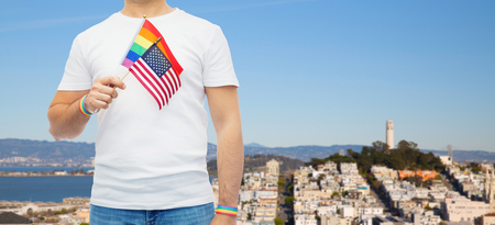 lgbt, same-sex relationships and homosexual concept - close up of man wearing gay pride rainbow awareness wristbands and holding american flag over san francisco city backgroundの写真素材