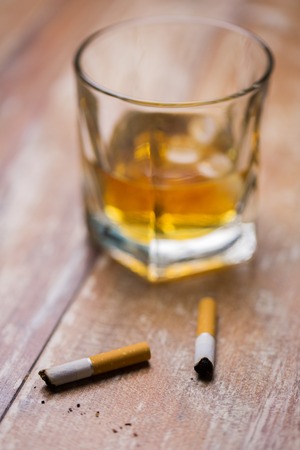 smoking and addiction concept - close up of cigarette butts and glass of alcohol on tableの写真素材