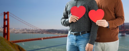 close up of happy male couple holding red hearts