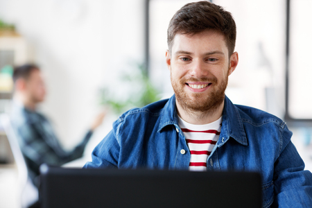 smiling creative man with laptop working at officeの写真素材