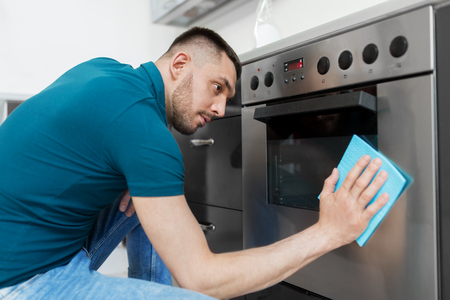 man with rag cleaning oven door at home kitchenの写真素材
