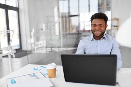 business, people and technology concept - african american businessman with laptop computer working at officeの写真素材