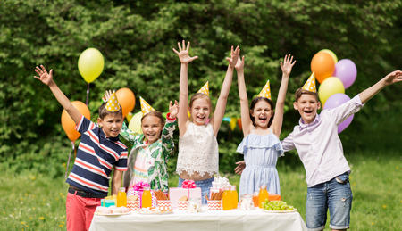 holidays, childhood and celebration concept - happy kids hugging on birthday party at summer gardenの写真素材