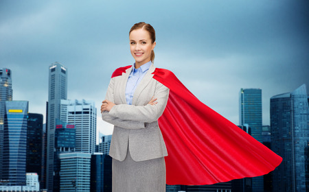 business, woman power and people concept - smiling businesswoman in red superhero cape over singapore city skyscrapers backgroundの写真素材