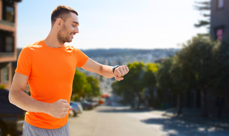 sport, technology and healthy lifestyle concept - smiling young man with smart watch or fitness tracker over san francisco city backgroundの写真素材
