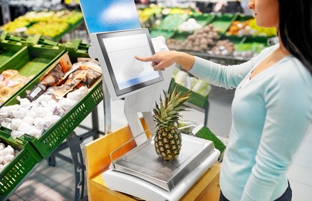 woman weighing pineapple on scale at grocery store