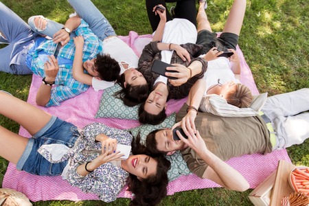 friends with smartphones on picnic blanketの写真素材