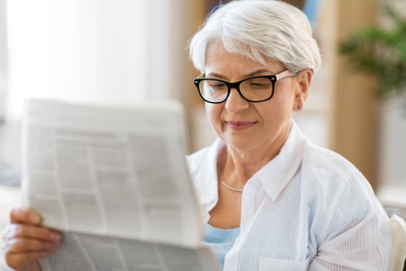 portrait of senior woman reading newspaper at homeの写真素材
