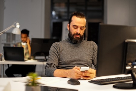 creative man with smartphone at night officeの写真素材