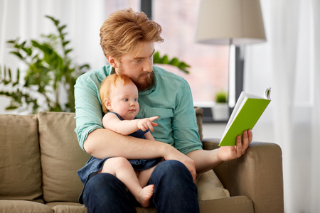 father reading book for baby daughter at homeの写真素材