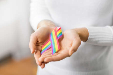 homosexual and lgbt concept - close up of female hands holding gay pride awareness ribbonの写真素材