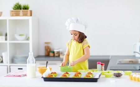 family, cooking, baking and people concept - little girl in chefs toque making batter for muffins or cupcakes at home kitchenの写真素材