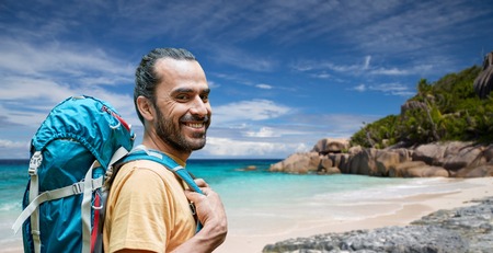 adventure, travel, tourism, hike and people concept - smiling man with backpack over background of seychelles island beach in indian oceanの写真素材