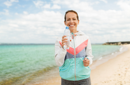 woman drinking water after exercising on beachの写真素材