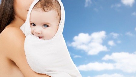 mother with baby in bath towel over sky backgroundの写真素材