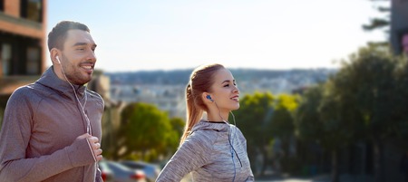 fitness, sport and technology concept - happy couple running and listening to music in earphones...