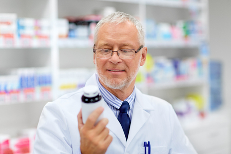medicine, healthcare and people concept - senior apothecary with drug at pharmacyの写真素材