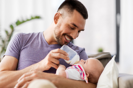 father feeding baby daughter from bottle at homeの写真素材