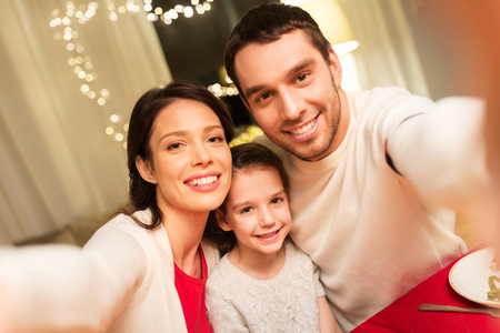 family, christmas and holidays concept - happy mother, father and little daughter taking selfie at homeの写真素材