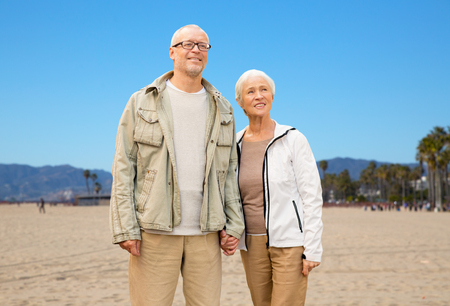 old age, travel and tourism and people concept - happy senior couple holding hands over venice beach background in californiaの写真素材
