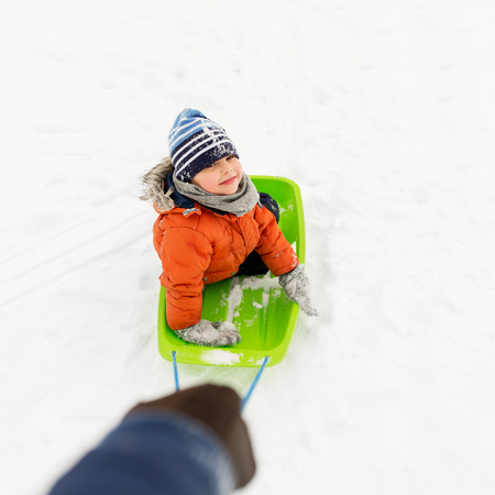 happy boy riding sled on snow in winterの写真素材