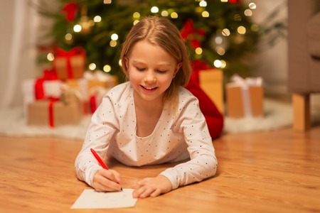 smiling girl writing christmas wish list at homeの写真素材