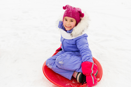 happy little girl with snow saucer sled in winterの写真素材