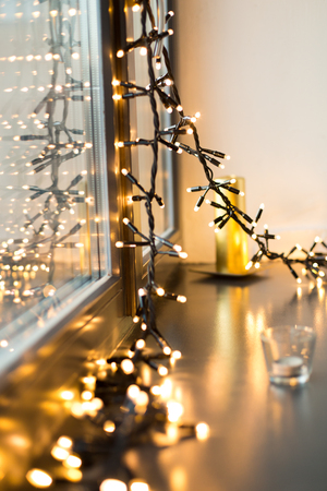 holidays and decoration concept - close up of christmas garland glowing on window sillの写真素材