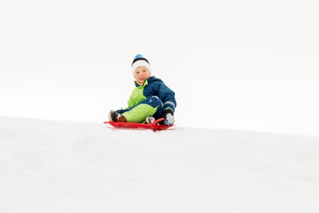 happy boy sliding on sled down snow hill in winter