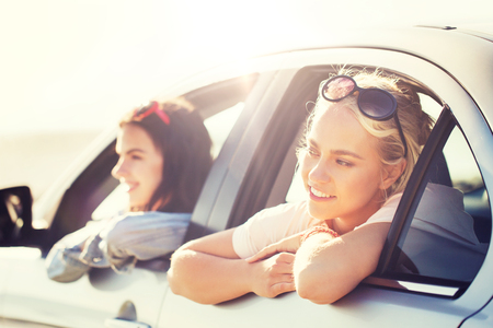 happy teenage girls or women in car at seasideの写真素材