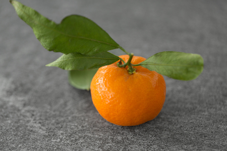 food, healthy eating and vegetarian concept - close up of whole mandarin with leaves on tableの写真素材
