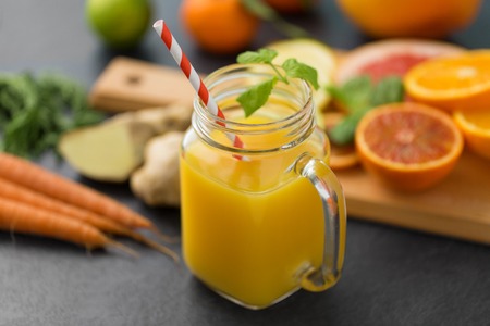 food , healthy eating and vegetarian concept - mason jar glass of orange juice with straw and citrus fruits on slate table topの写真素材
