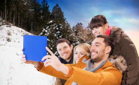 people, technology and leisure concept - happy friends taking selfie by tablet pc computer over winter backgroundの写真素材