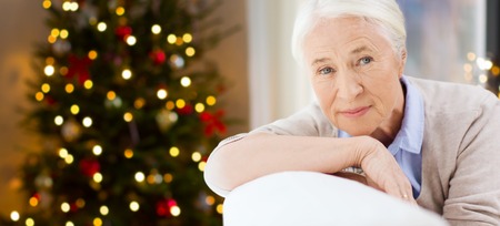 holidays, age and people concept - happy smiling senior woman at home over christmas tree lights backgroundの写真素材