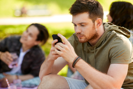leisure, technology and people concept - woman using smartphone at picnic with friends in summer parkの写真素材