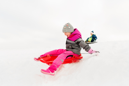 happy little girl sliding down on sled in winterの写真素材